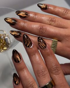 Mãos de pele preta, com anéis em dourado e unha amendoada estampa de animal print