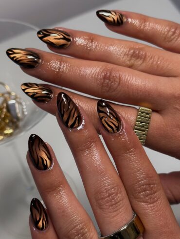 Mãos de pele preta, com anéis em dourado e unha amendoada estampa de animal print