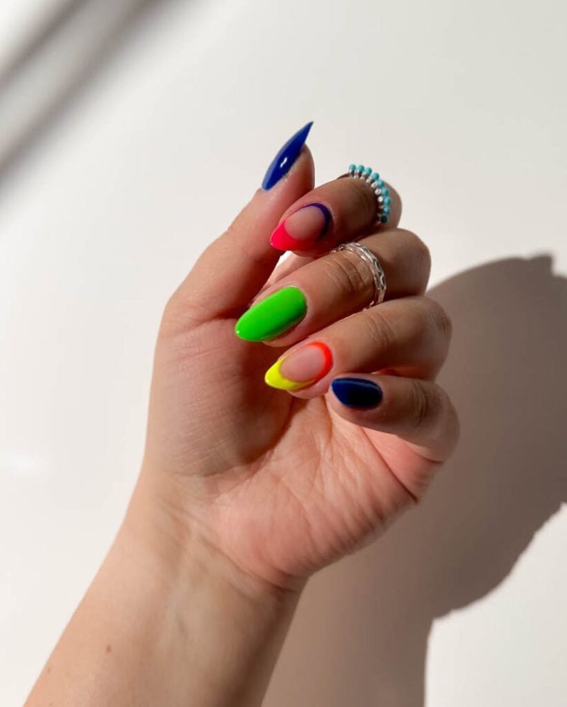 Mão de pele clara, com anéis e unha amendoada neon