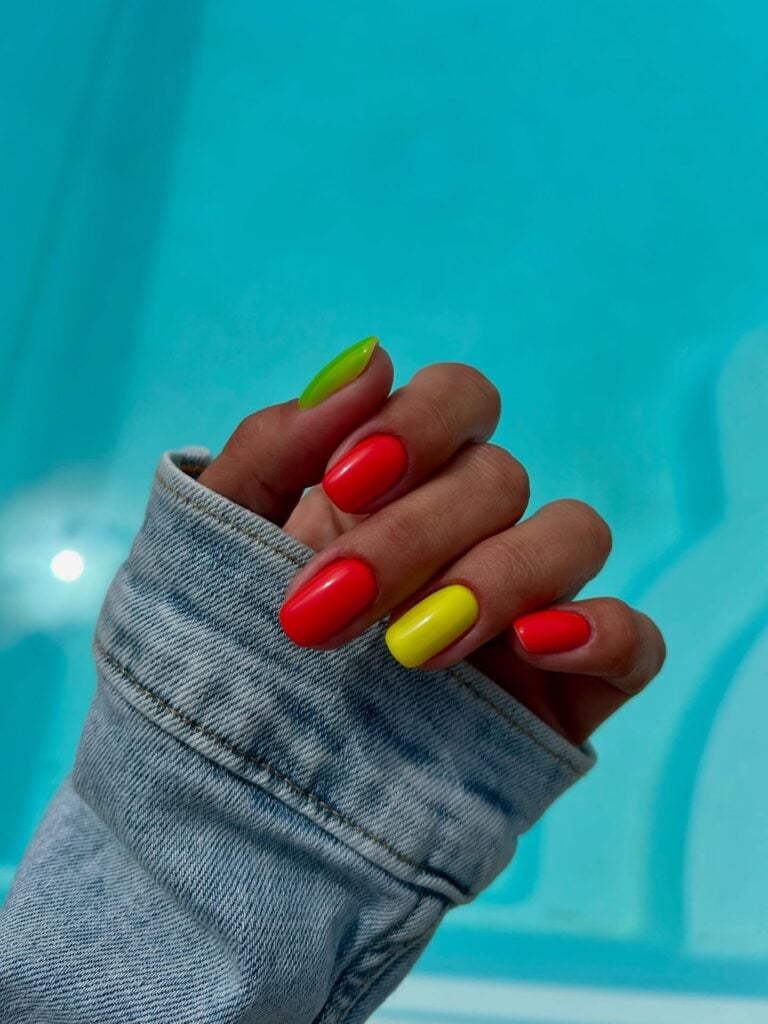 Unhas com esmalte laranja, amarelo e verde em mão de pele branca