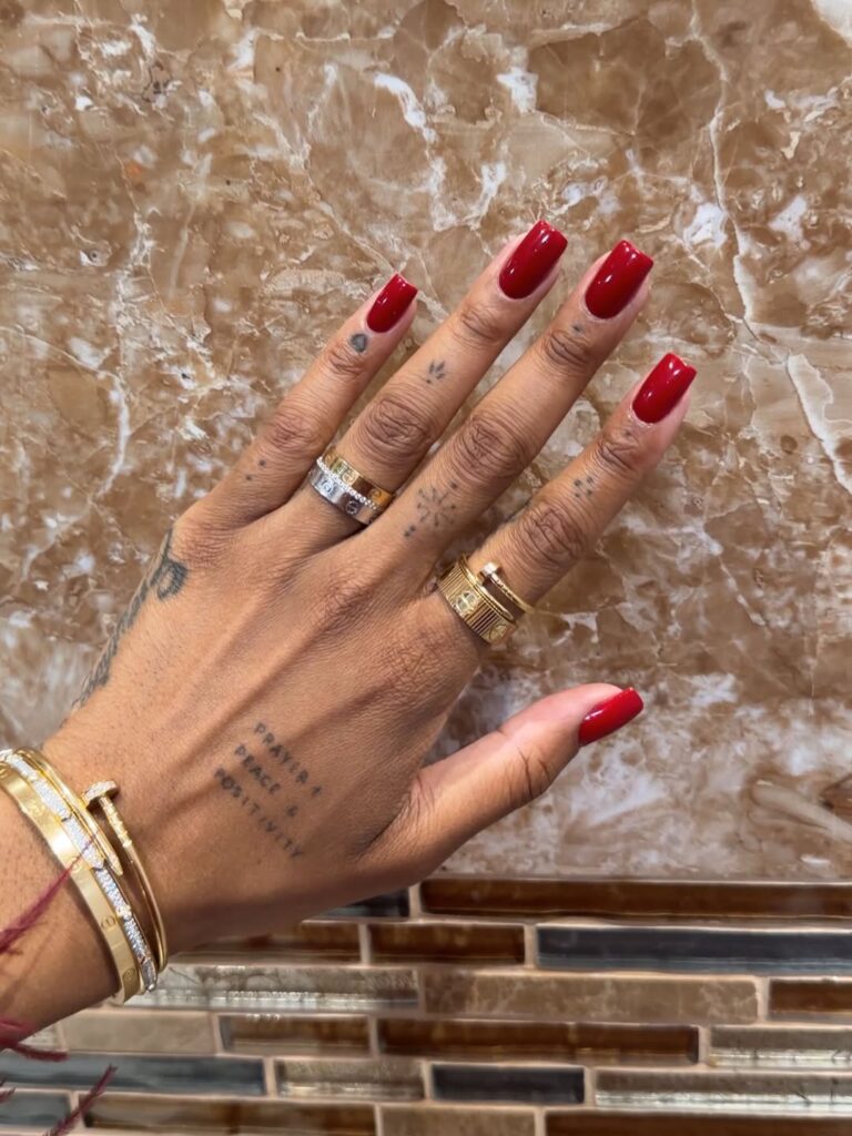 Mão de pele clara, com anéis em dourado e unha quadrada com esmalte vermelho-escuro