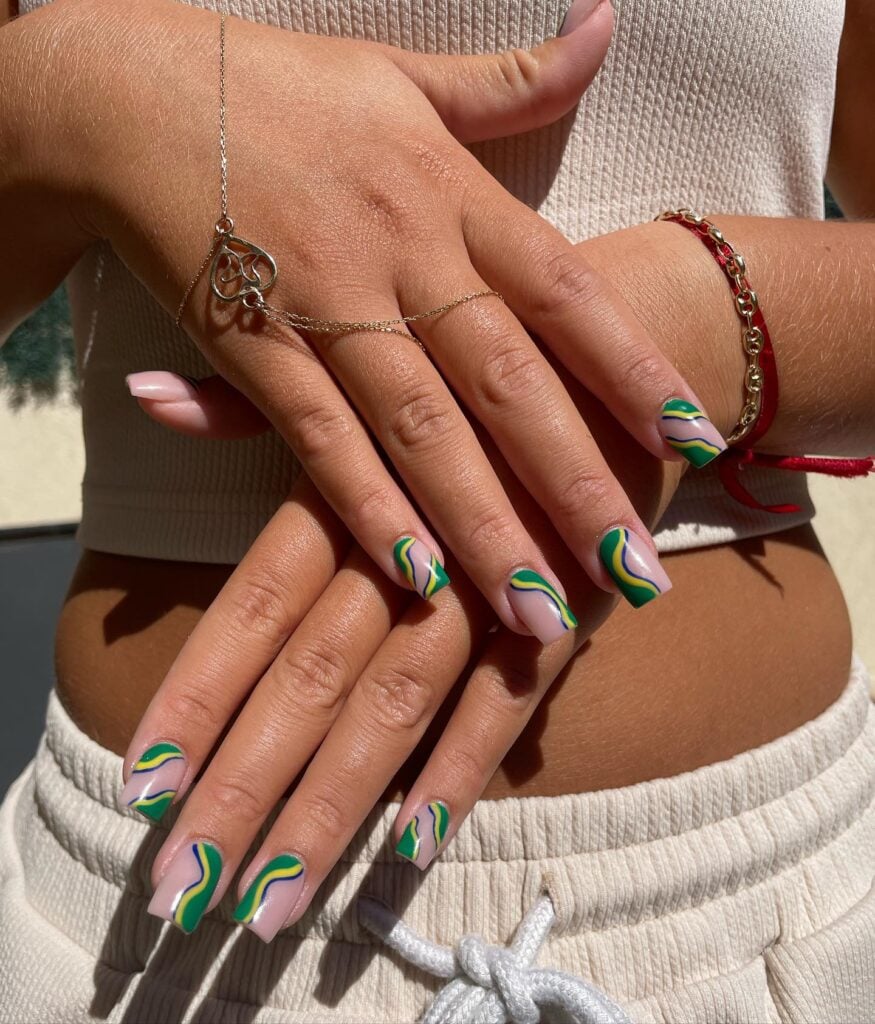 Unhas com esmalte azul, amarelo e verde em mão de pele branca