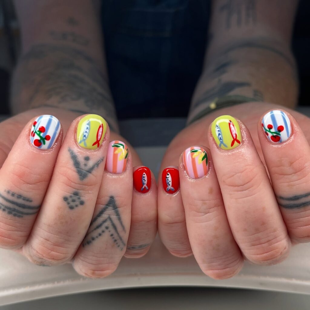 Unhas curtas com técnica de nail art maximalista com listras, tomate, limão siciliano e sardinha em mão de pele branca