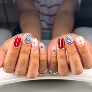 Unha curta com nail art maximalista em mão de pele negra com esmalte vermelho, azul e branco