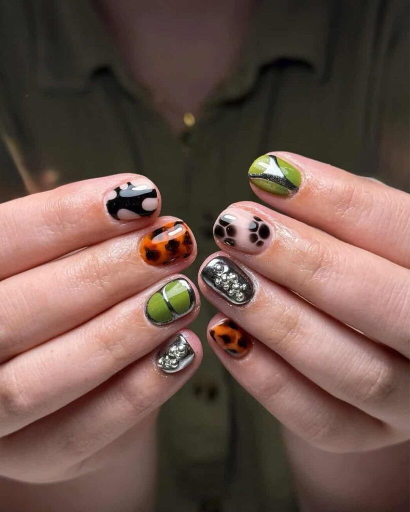 Unha curta com nail art maximalista em mão de pele branca com esmalte preto, laranja e verde com metalizado e cromado
