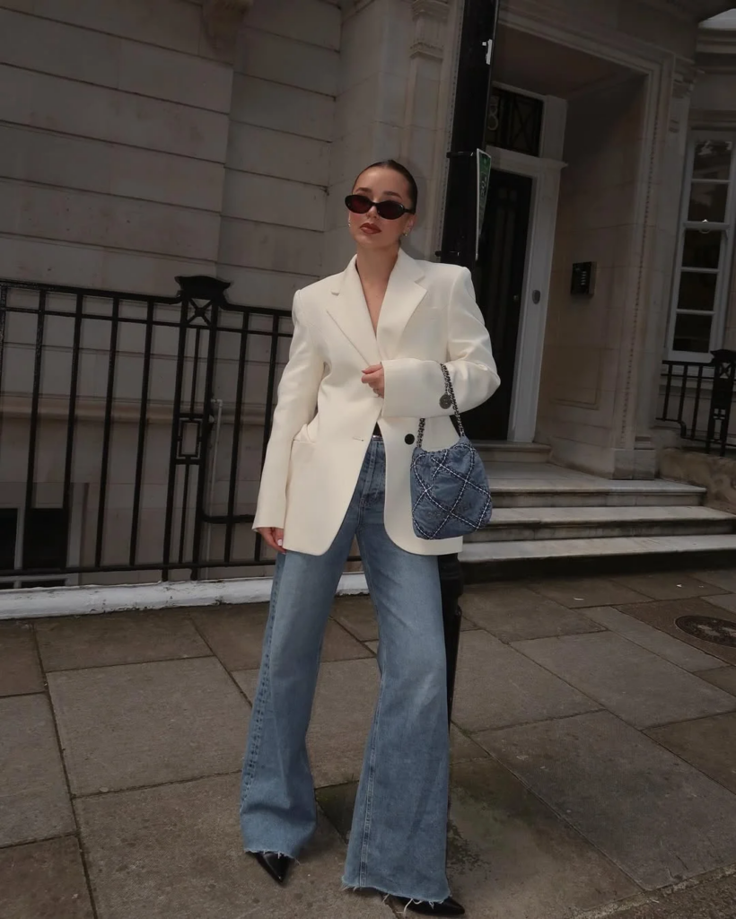 Mulher jovem, magra e de pele clara com blazer claro e calça jeans