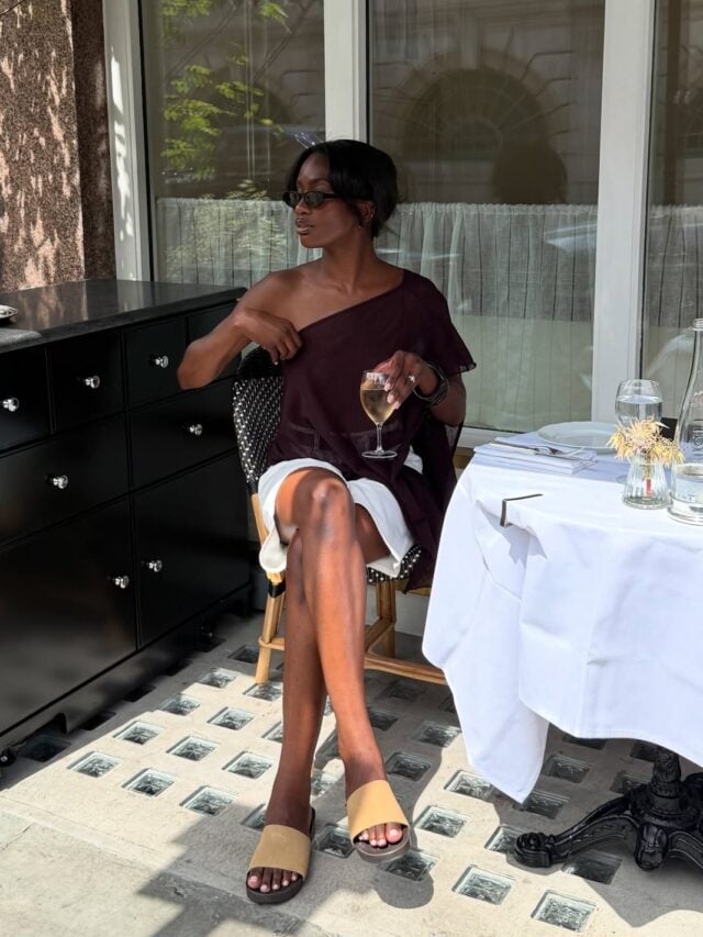 Look de trabalho com blusa assimétrica marrom e short branco de alfaiataria em mulher negra