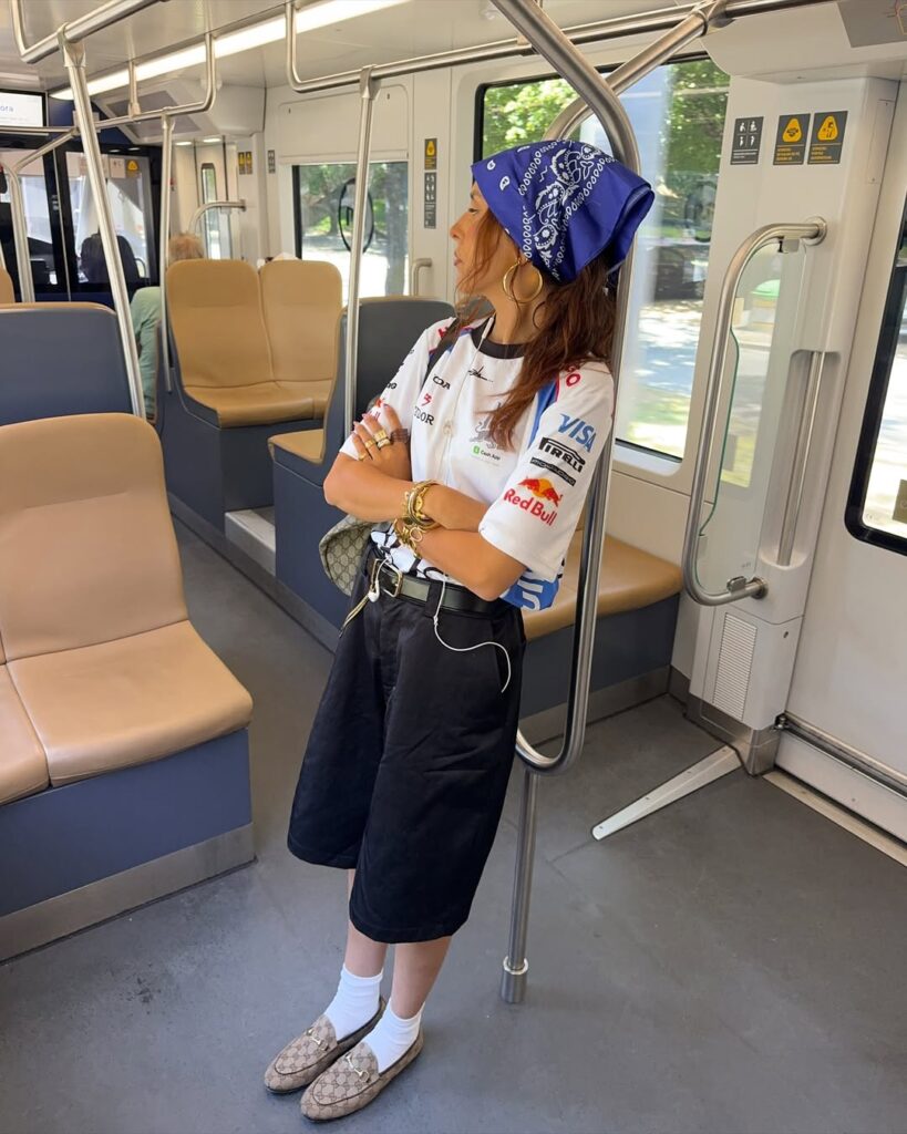 Mulher jovem, magra e de pele clara. Ela usa camiseta esporiva, bermuda e mocassim