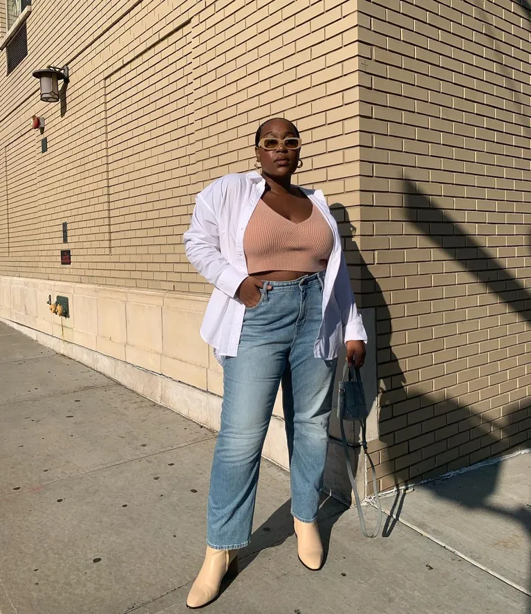 Mulher jovem de pele negra usando top, calça mom jeans, camisa branca e botas