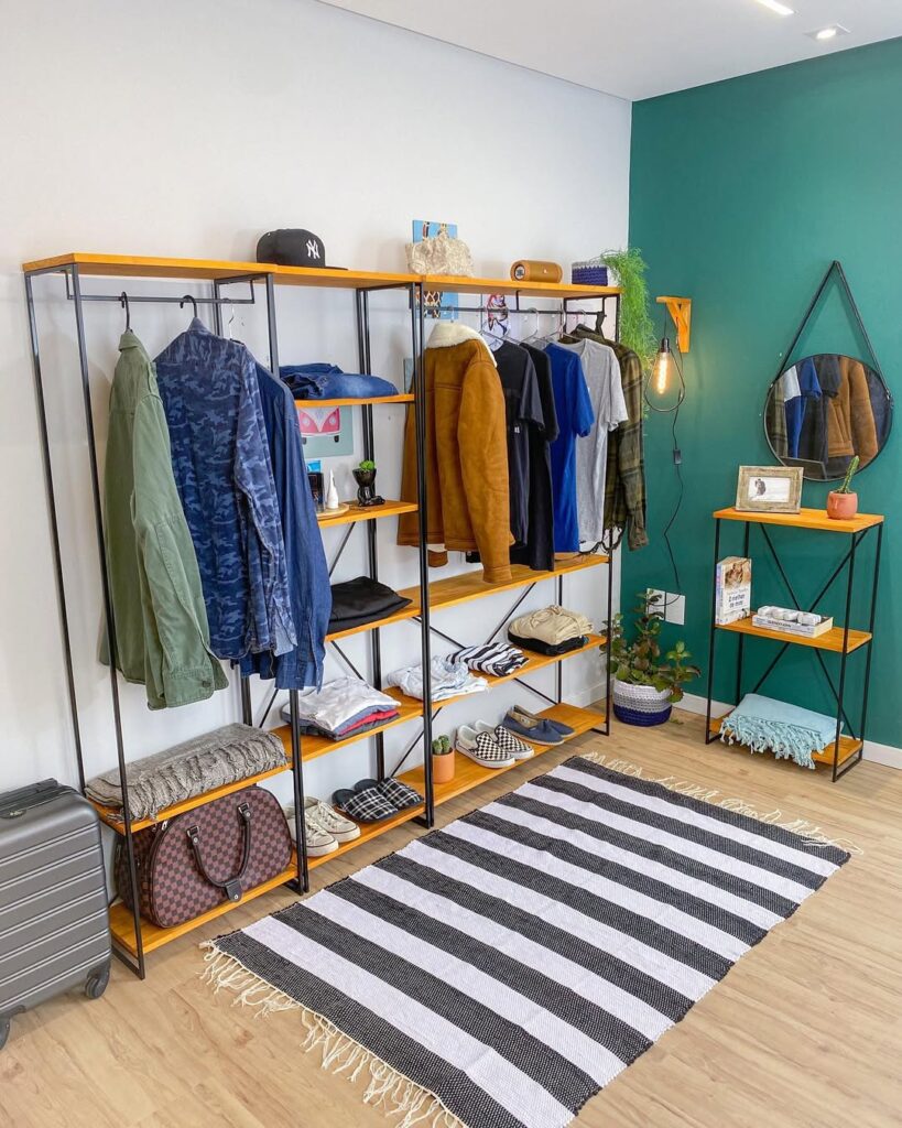 Arara de roupas com prateleiras em ambiente com parede verde, espelho Adnet e tapete listrado