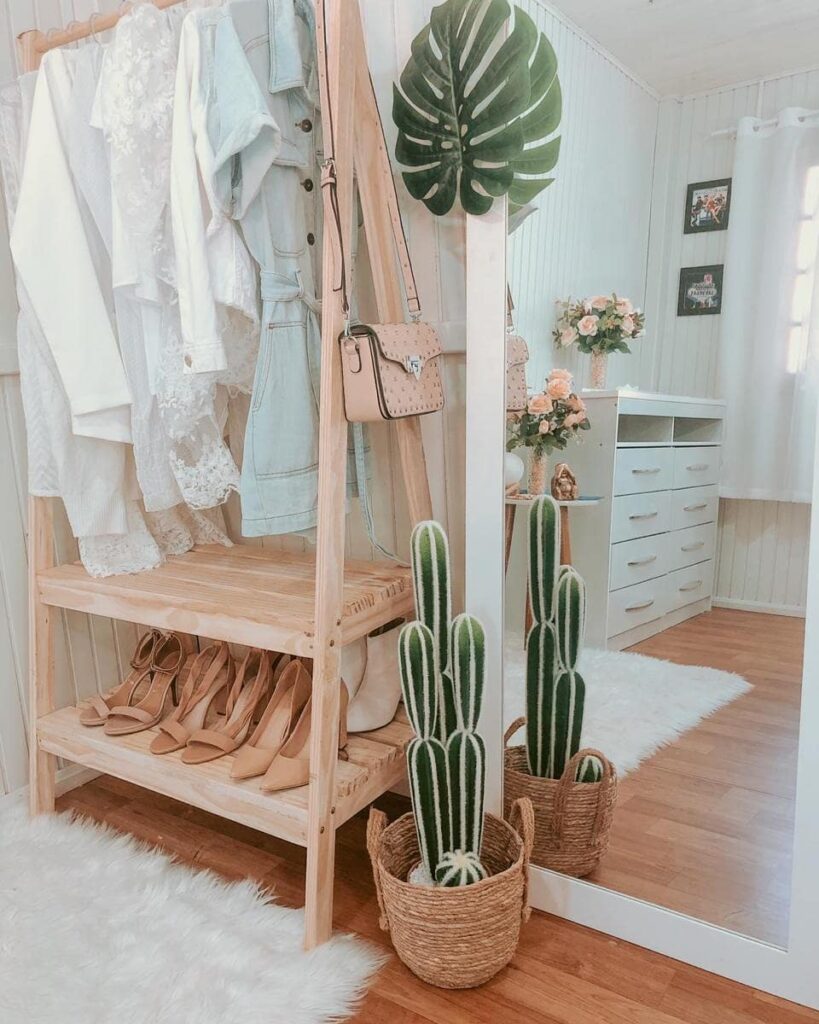 Arara de roupas de madeira clara com sapateira, com roupas claras e cactus ao lado