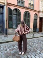 Mulher de pele clara, com camisa listrada e calça barrel marrom