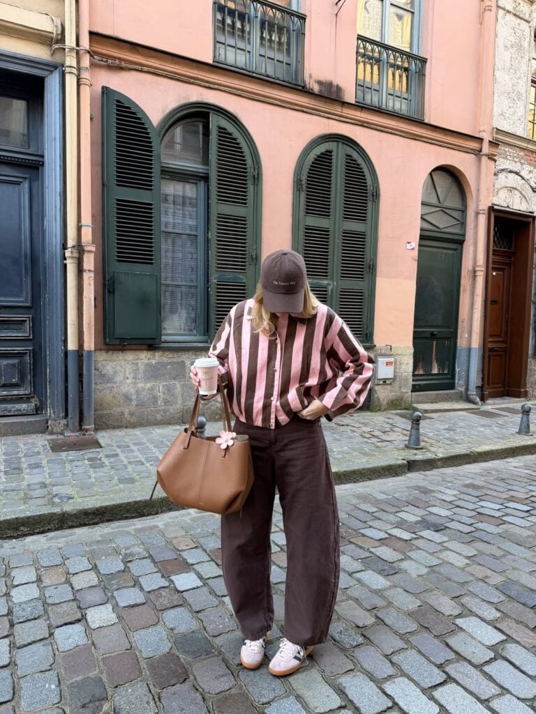 Mulher de pele clara, com camisa listrada e calça barrel marrom