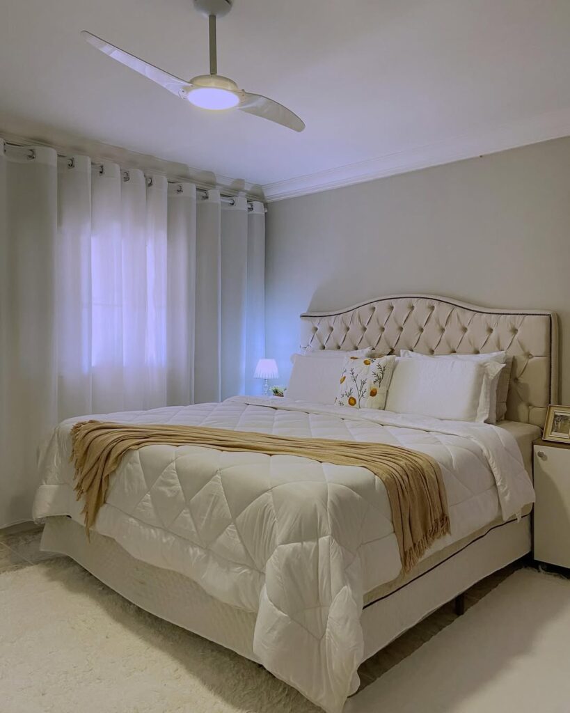 Cama de casal com cabeceira branca em capitonê com almofadas e colcha branca