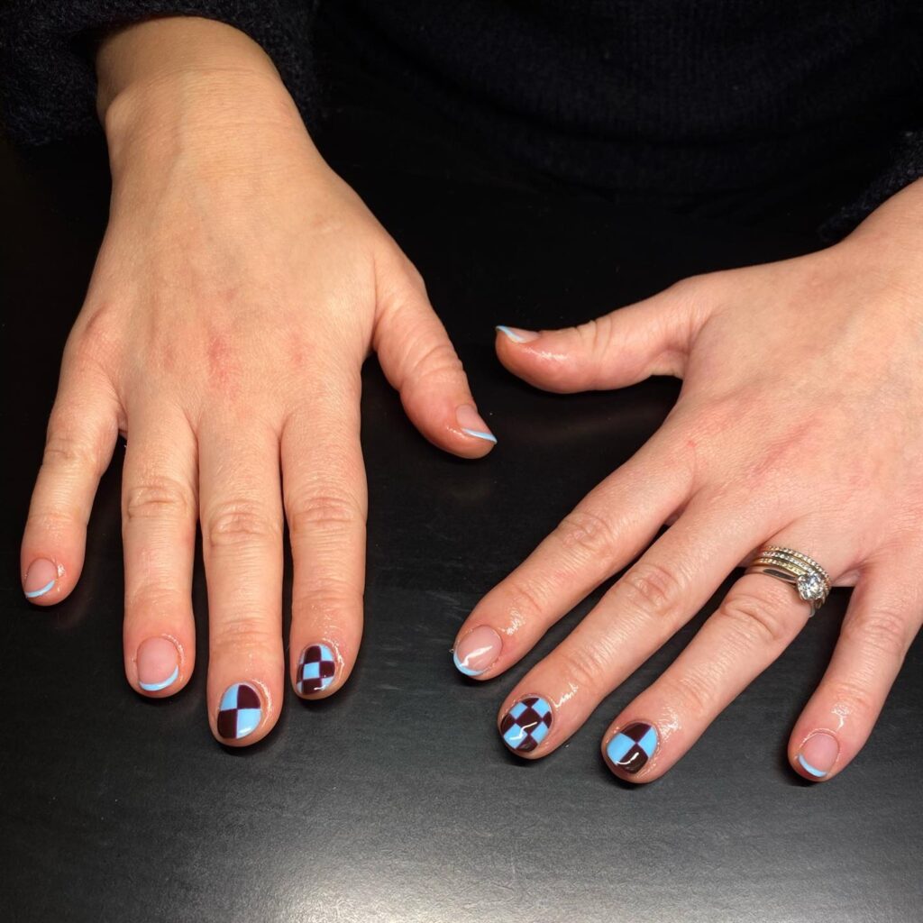 Mão de pele branca com unha azul e marrom com checkerboard nails ou unhas de tabuleiro de xadrez com efeito quadriculado e francesinha