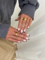 Mãos de pele clara, com anéis em dourado e unha amendoada com francesinha