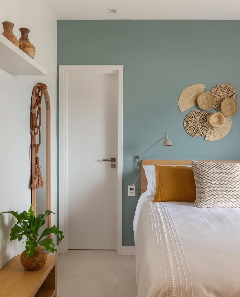 Quarto com parede azul-claro atrás da cama e itens de palha na decoração