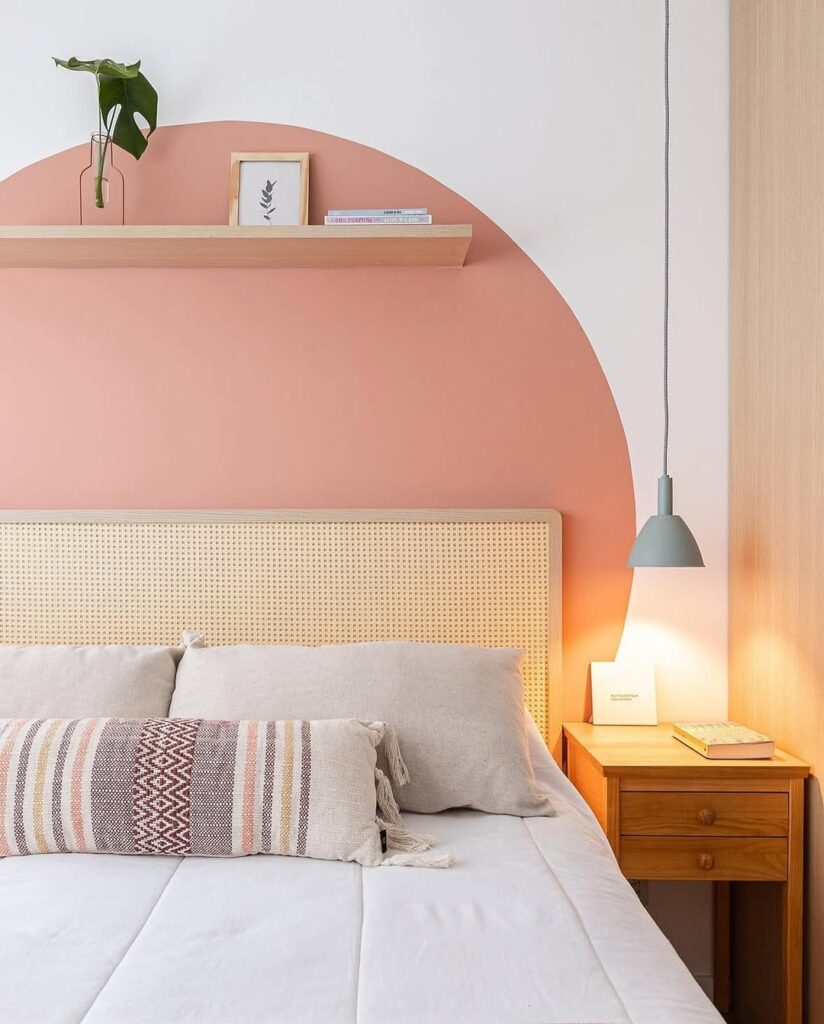 Quarto com cabeceira de palhinha e pintura em formato circular rosa na parede e prateleira de madeira