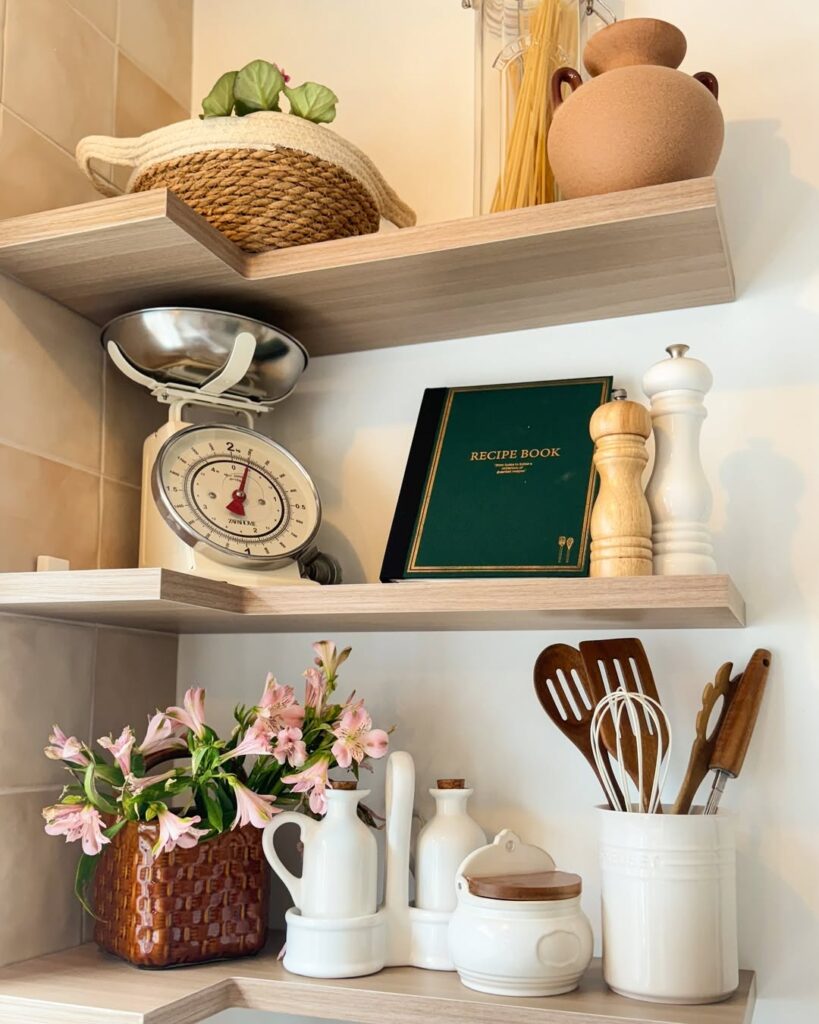 Cozinha com prateleiras no canto, balança, livro de receitas e utensílios de cozinha