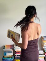 Mulher de pele clara, com roupa marrom e cabelo preso. Ela está segurando um livro