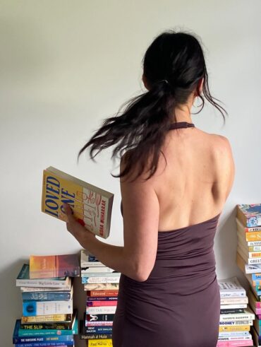 Mulher de pele clara, com roupa marrom e cabelo preso. Ela está segurando um livro