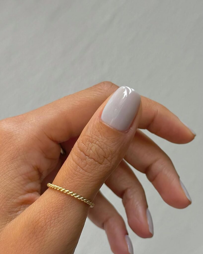 Mão de pele clara, com anel dourado e unha quadrada cinza