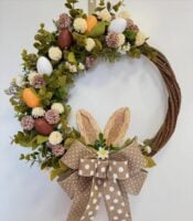 Guirlanda de Páscoa com galhos retorcidos, ovinhos, folhas, florzinhas e laços bege com bolinhas brancas