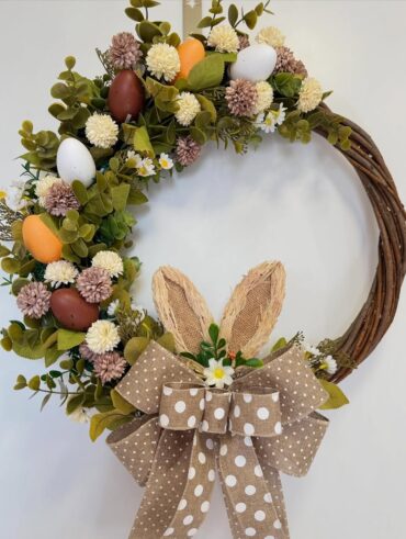 Guirlanda de Páscoa com galhos retorcidos, ovinhos, folhas, florzinhas e laços bege com bolinhas brancas