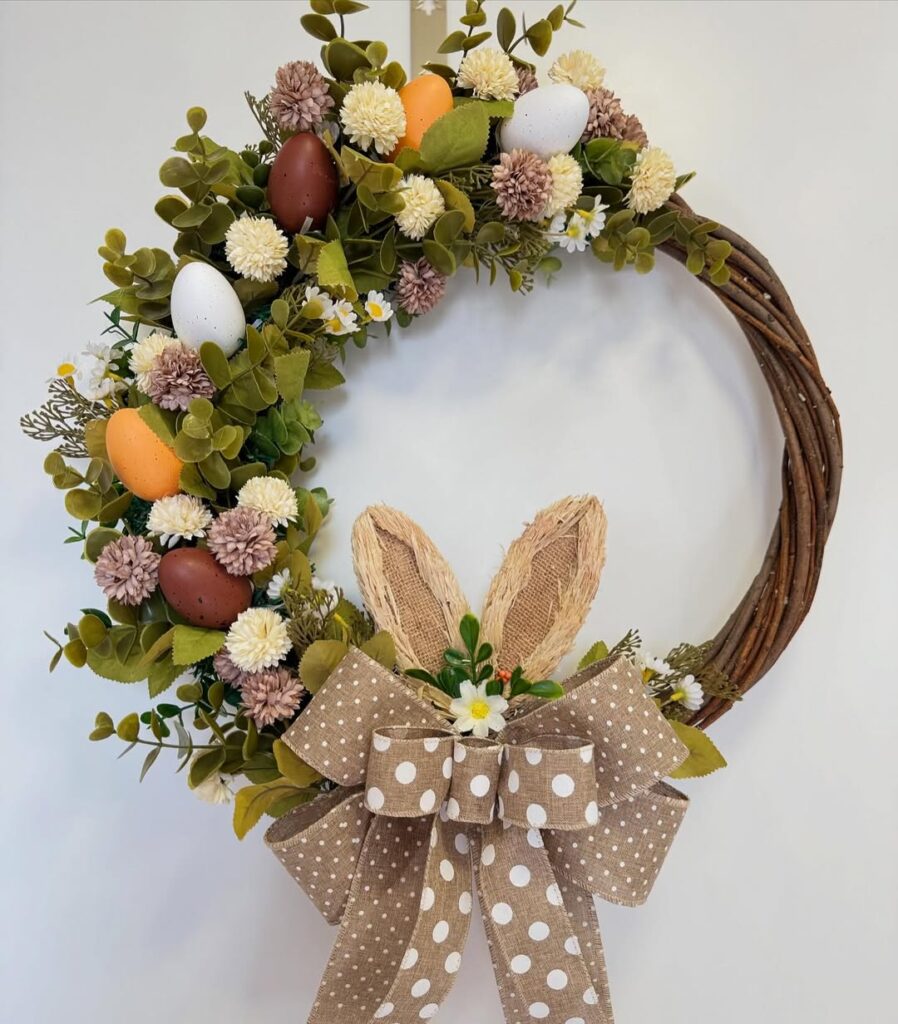 Guirlanda de Páscoa com galhos retorcidos, ovinhos, folhas, florzinhas e laços bege com bolinhas brancas