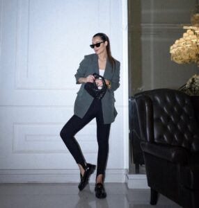 Mulher de pele clara, com calça fusô preta e blazer cinza