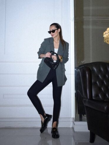 Mulher de pele clara, com calça fusô preta e blazer cinza