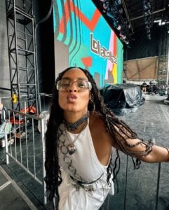 Mulher de pele preta, com look branco e cabelo trançado