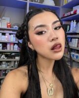 Mulher de pele clara, com cabelo preto em penteado e maquiagem com pérolas