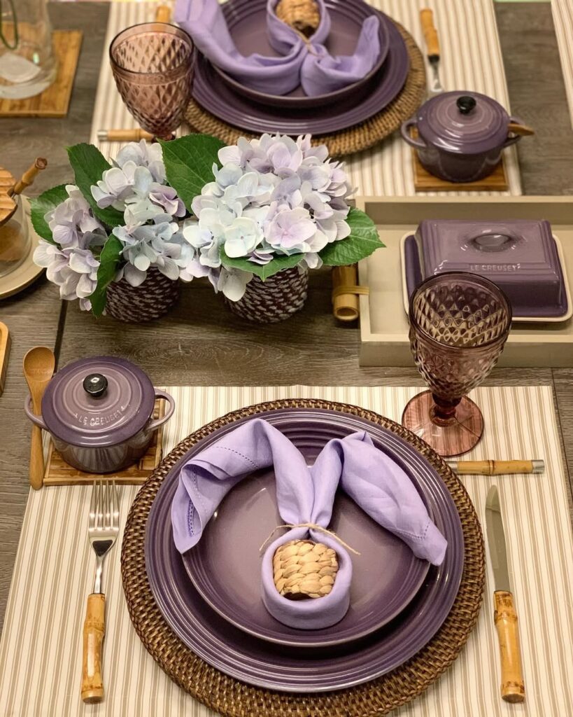 Mesa posta com louças em tom de roxo, arranjos com flores e guardanapo arrumado em formato de coelho