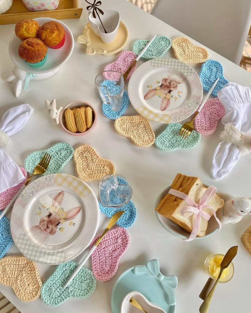Mesa de Páscoa com sousplats de crochê com corações coloridos, pratos com coelhos e talheres dourados