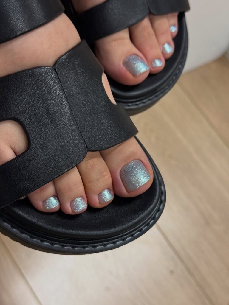 Pés de pele clara, com unhas pratas brilhosas