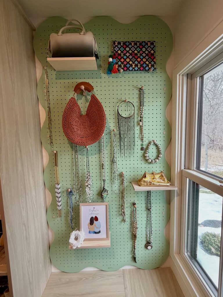 Pegboard verde com prateleiras, colares, bolsa e quadrinho