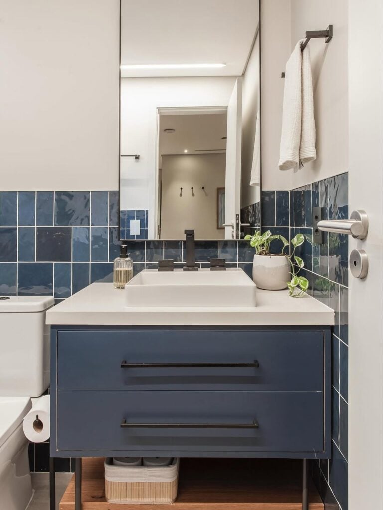 Banheiro com revestimento azul, balcão azul com bancada branca e puxadores pretos