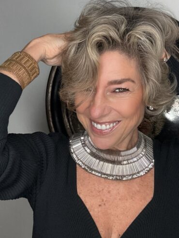 Mulher de pele clara, com blusa preta, cabelo curto e pele madura