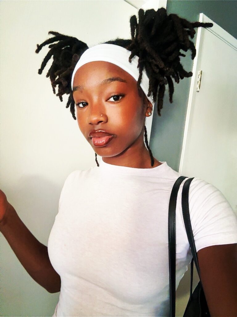 Mulher de pele preta, com blusa branca e cabelo com penteado space bun