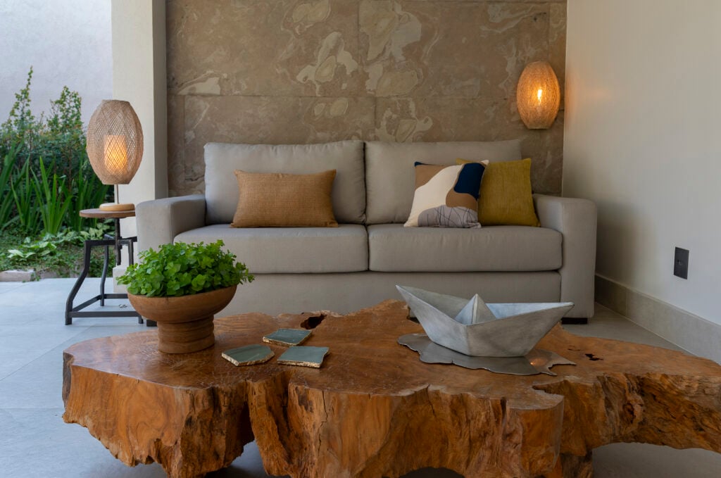 Sala com sofá cinza de linhas retas, luminárias de fibra natural e mesa de madeira em formato orgânico