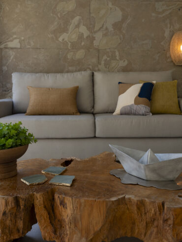 Sala com sofá cinza de linhas retas, luminárias de fibra natural e mesa de madeira em formato orgânico