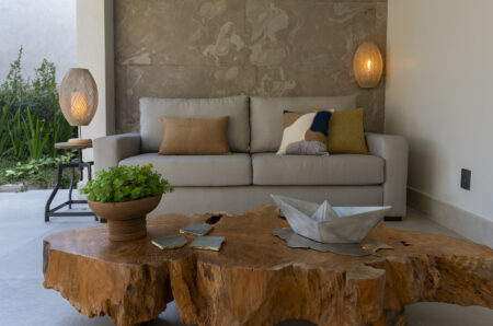 Sala com sofá cinza de linhas retas, luminárias de fibra natural e mesa de madeira em formato orgânico