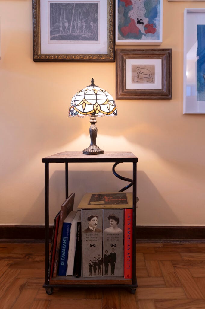 Móvel com abajur vintage com livros embaixo e quadros na parede