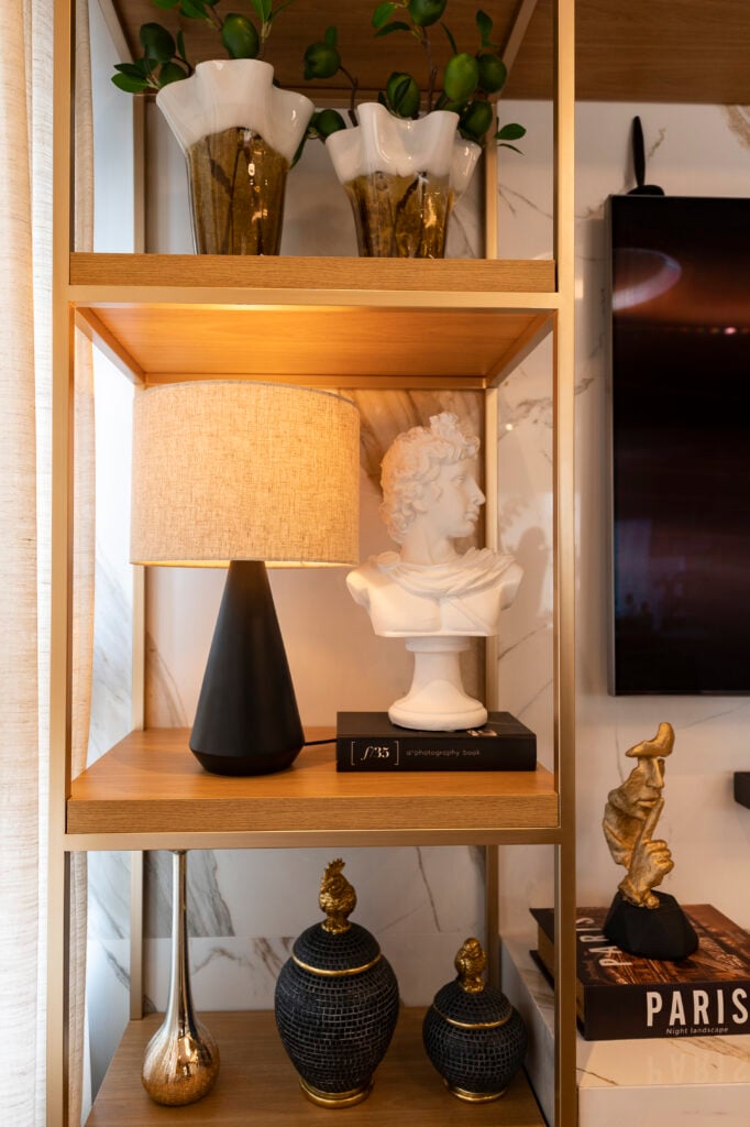Estante com abajur de base preta e outros objetos decorativos