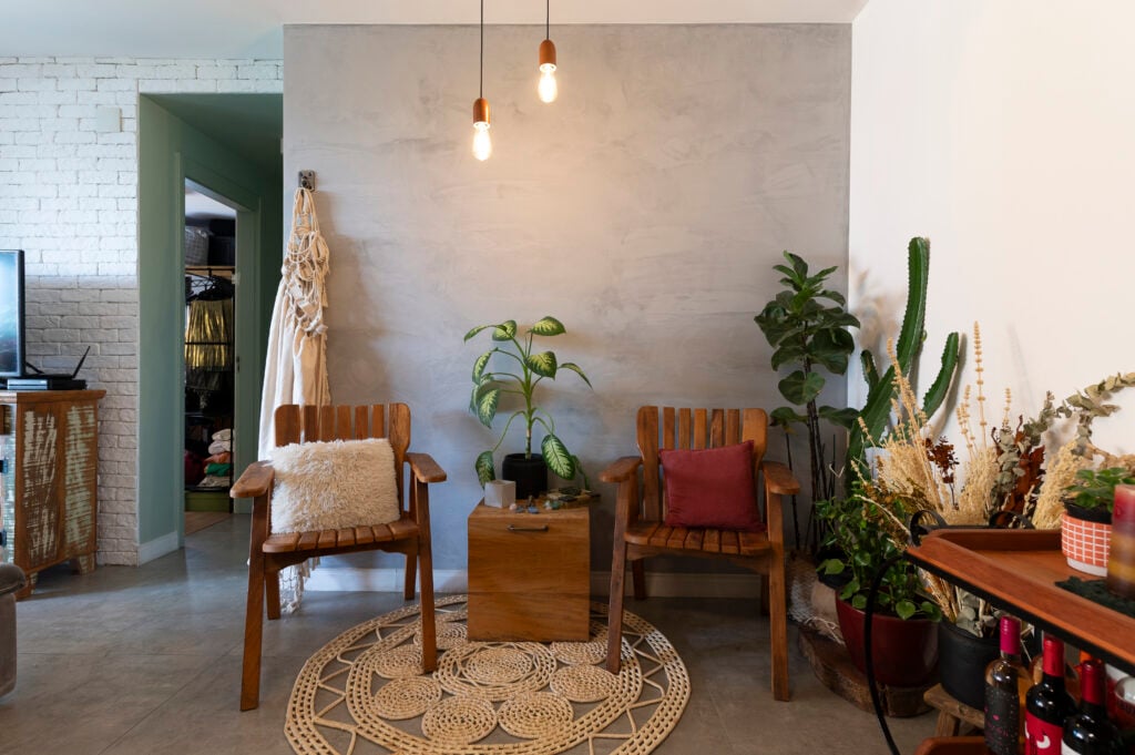 Sala de estar com cadeiras de madeira, tapete de crochê e plantas variadas