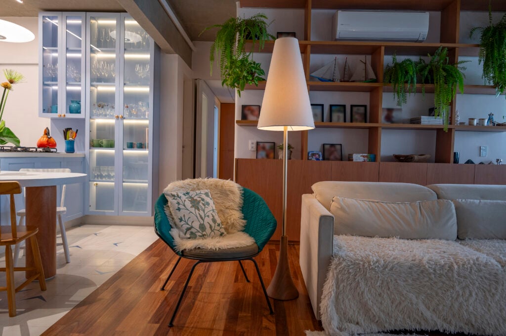 Sala de estar com sofá claro, luminária de piso e poltrona azul com base de metal preto