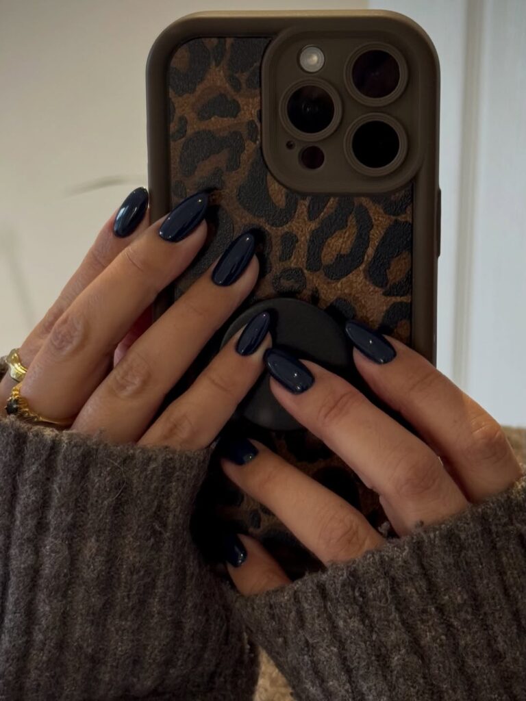 Mãos de pele clara, com anel em dourado e unhas amendoadas azul-marinho