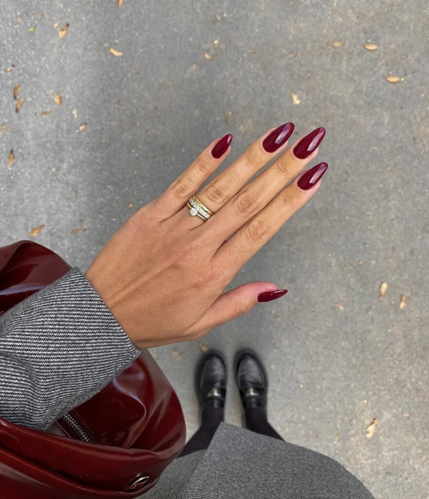Mão de pele clara, com anéis e unha amendoada burgundy