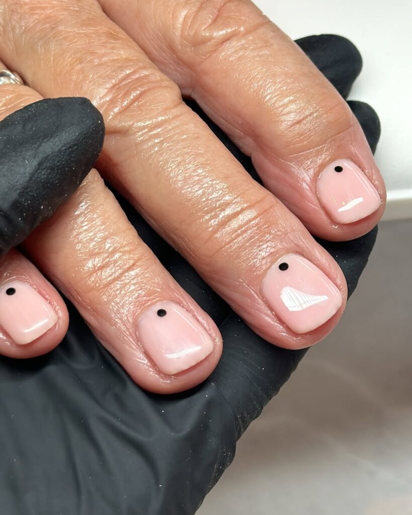 Mão de pele clara, com unha neutra com bolinha preta 